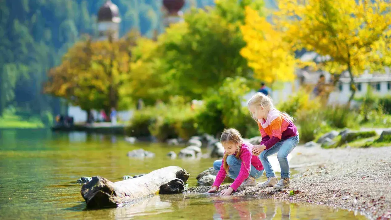 Zwei Mädchen genießen ihren Urlaub mit Kindern in Bayern am See. Sie spielen am Ufer im bunten Herbstlaub.