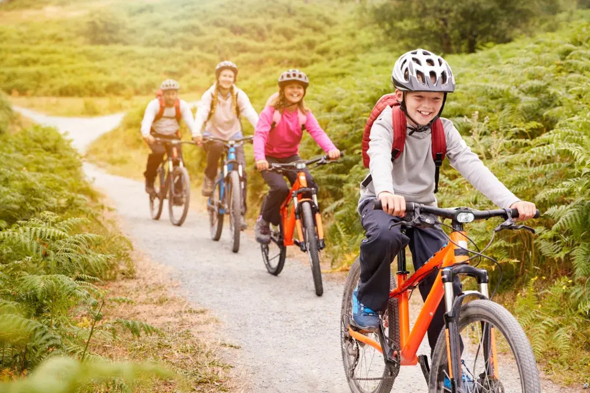 Fröhliche Familie auf einer Fahrradtour mit Kindern durch eine grüne Landschaft.