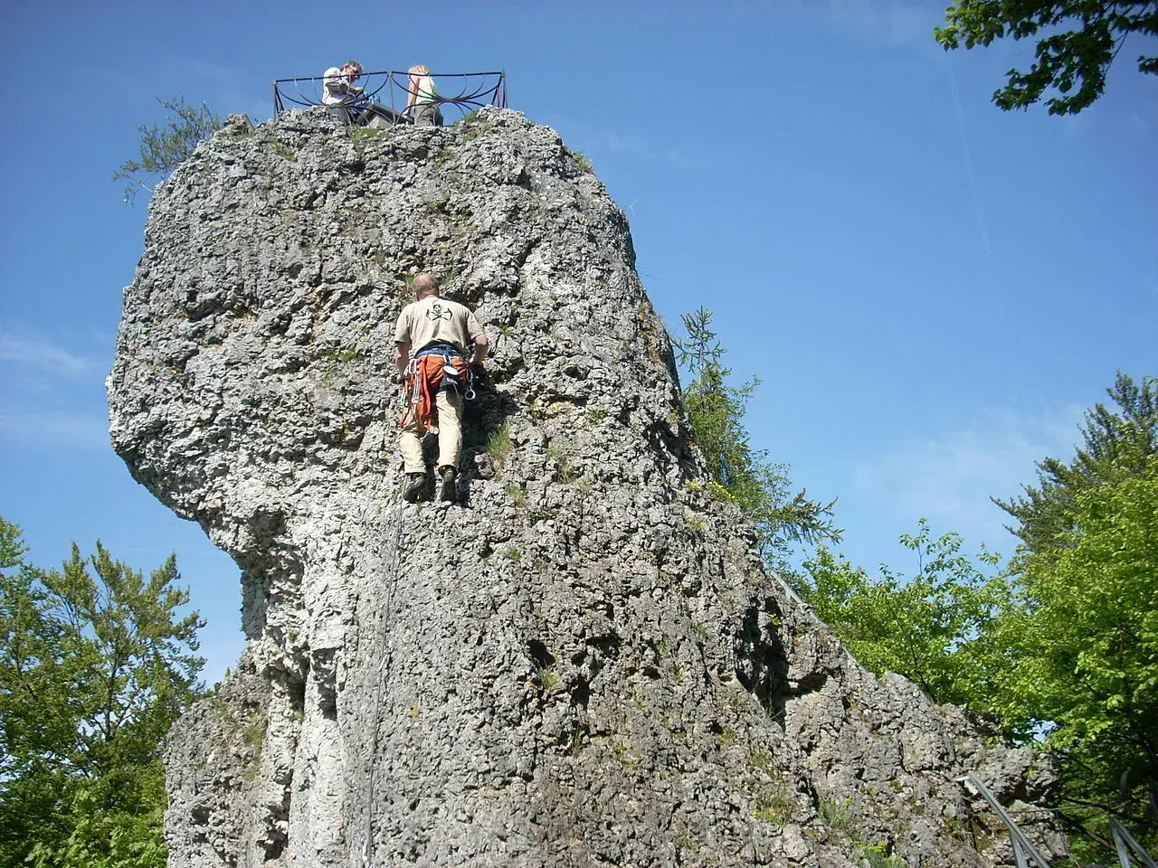 Kletterer erklimmt Felsen bei der Burgruine Wolfsberg. Oben genießen zwei Personen die Aussicht.