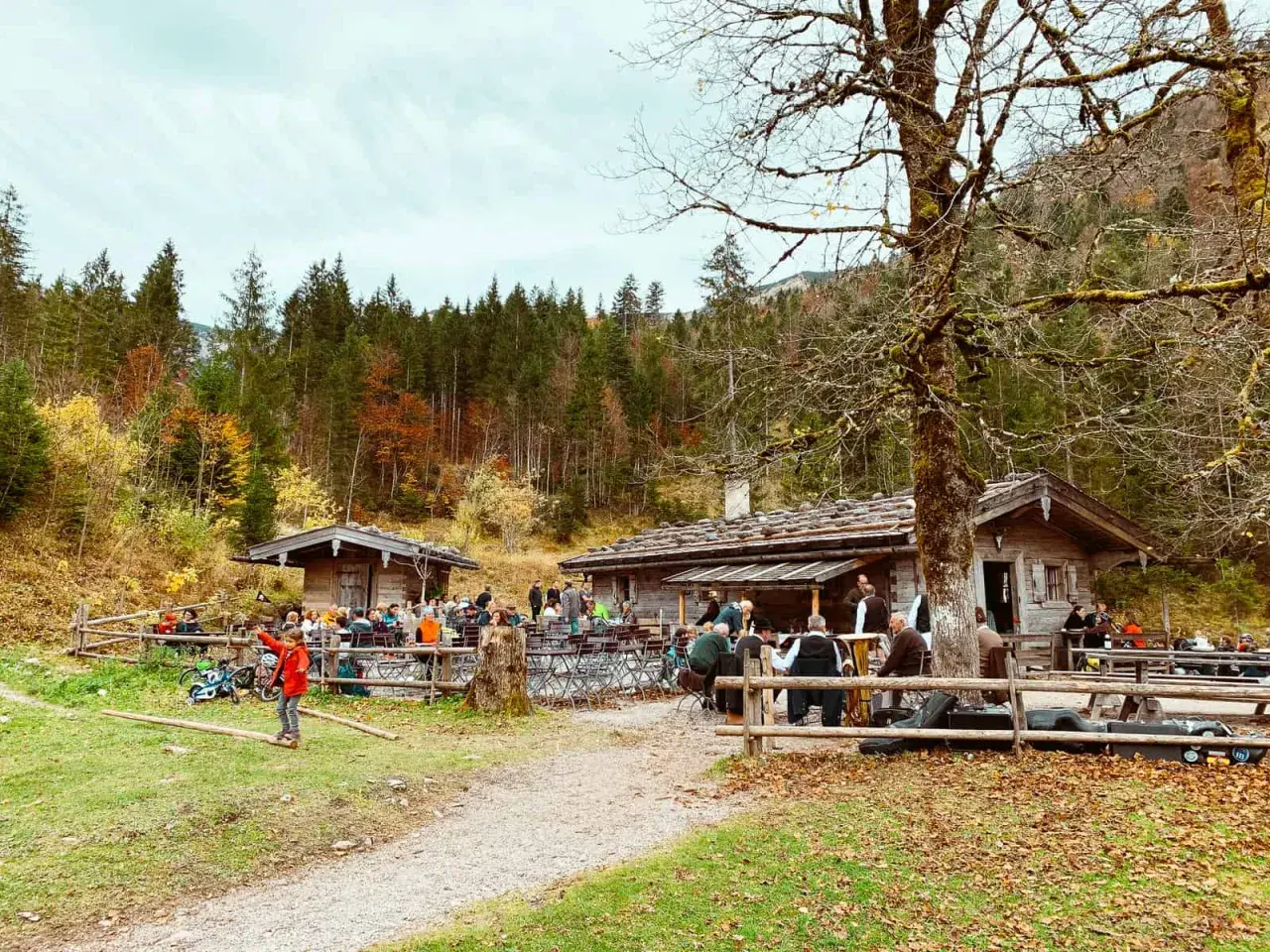 Familien genießen einen Herbsttag am Tegernsee. Kinder spielen im Gras, während Erwachsene in gemütlichen Hütten sitzen.
