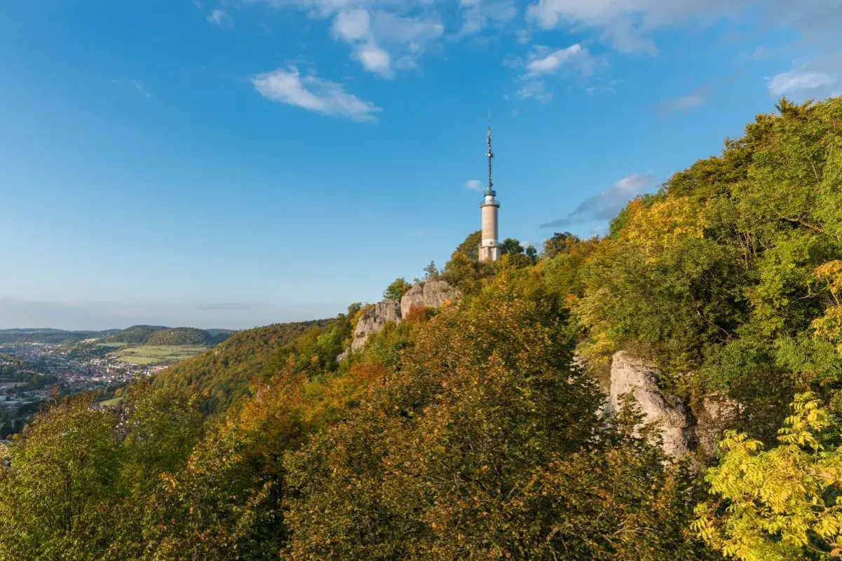 Der Schlossfelsenturm Albstadt ragt auf einem bewaldeten Felsen über der Stadt auf. Bunte Herbstfarben schmücken die Hänge.