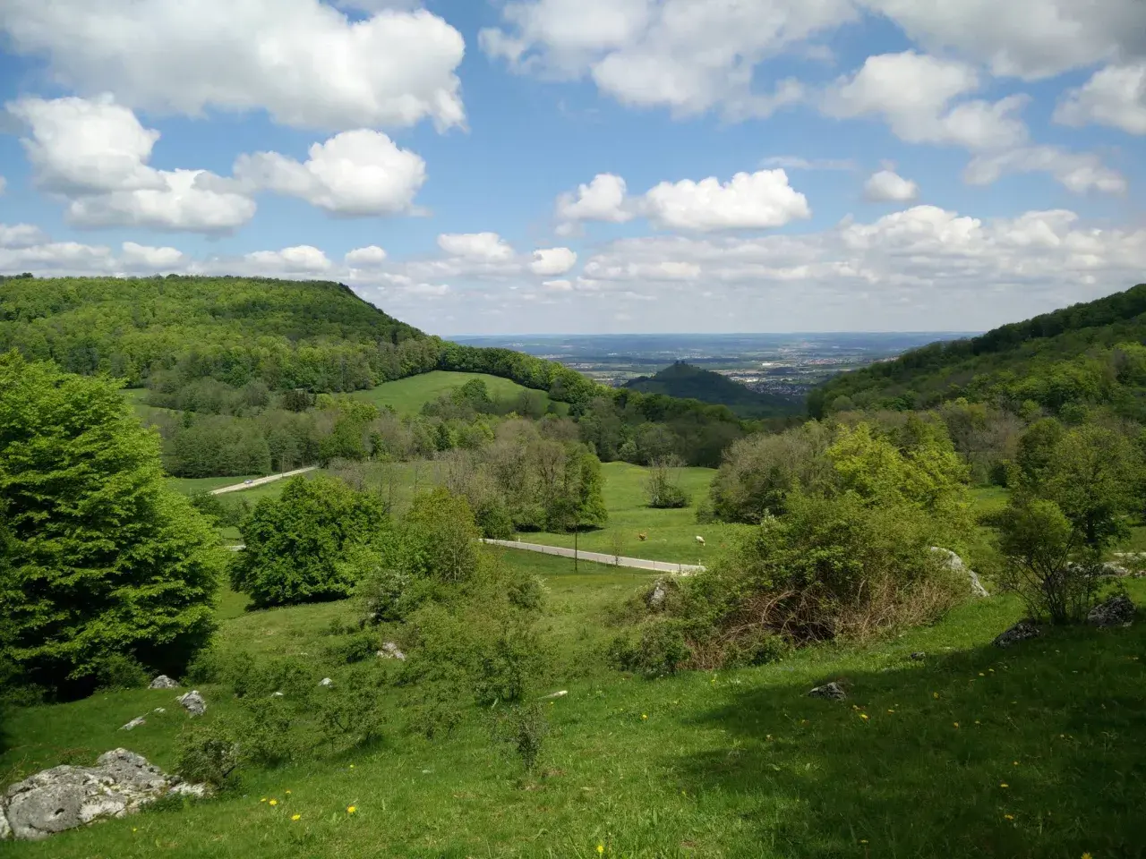 Grüne Hügel und Wiesen, ideal für eine Randecker Maar Wanderung. Wolken ziehen über das weite Tal.