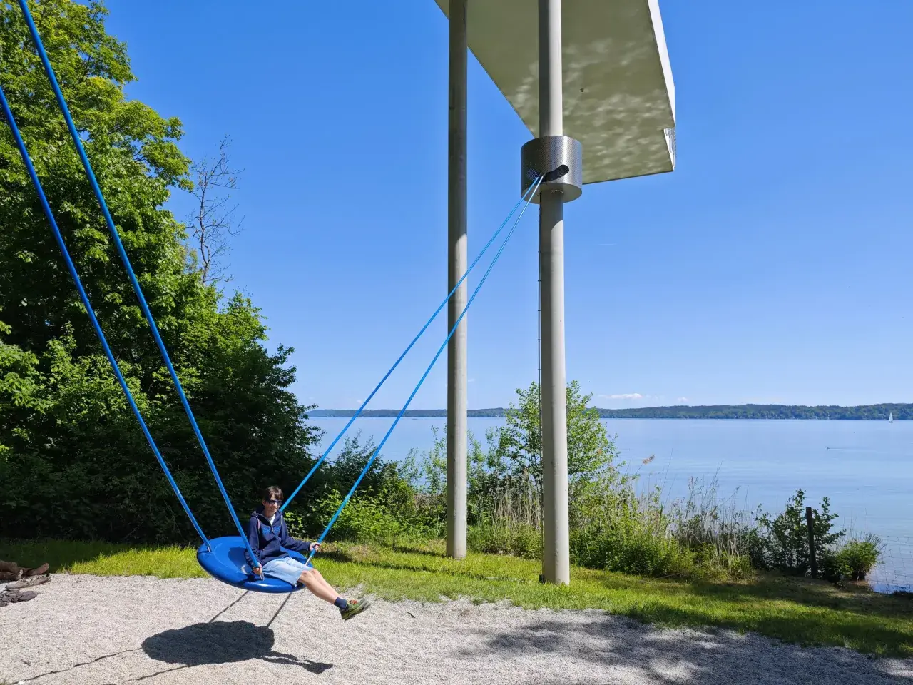 Ein Junge schaukelt am Starnberger See. Kinder genießen die Sonne und den Blick auf das Wasser.