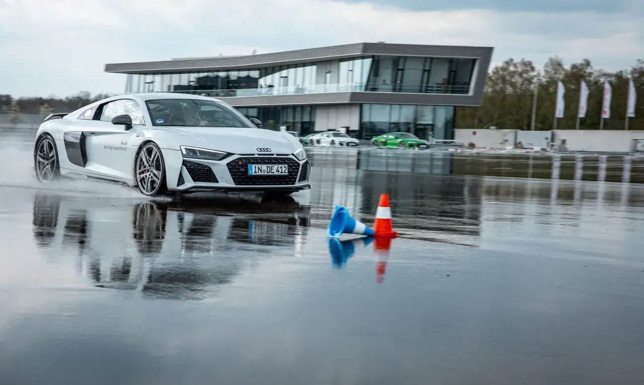 Ein weißer Audi R8 fährt auf nasser Strecke. Hier kann man in Ingolstadt das Fahren auf Eis und Schnee trainieren.