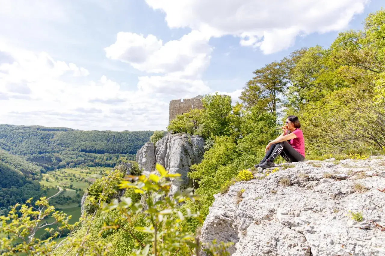 Frau genießt Aussicht bei einer Filsursprung Wanderung. Ruine thront über bewaldetem Tal.