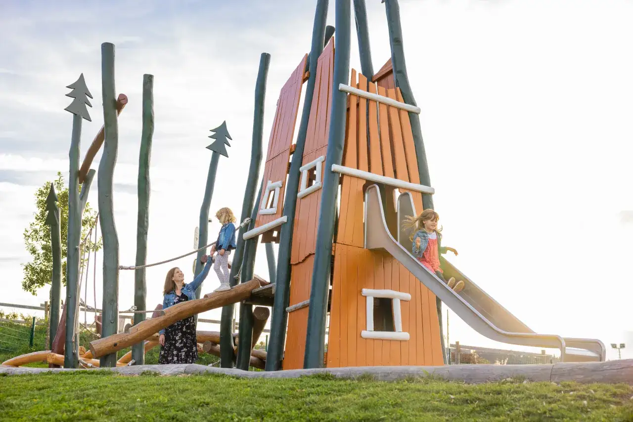 Familie genießt einen sonnigen Tag auf einem Abenteuerspielplatz. Kinder klettern und rutschen, während die Mutter zusieht. Perfekt für Winterberg mit Kindern.