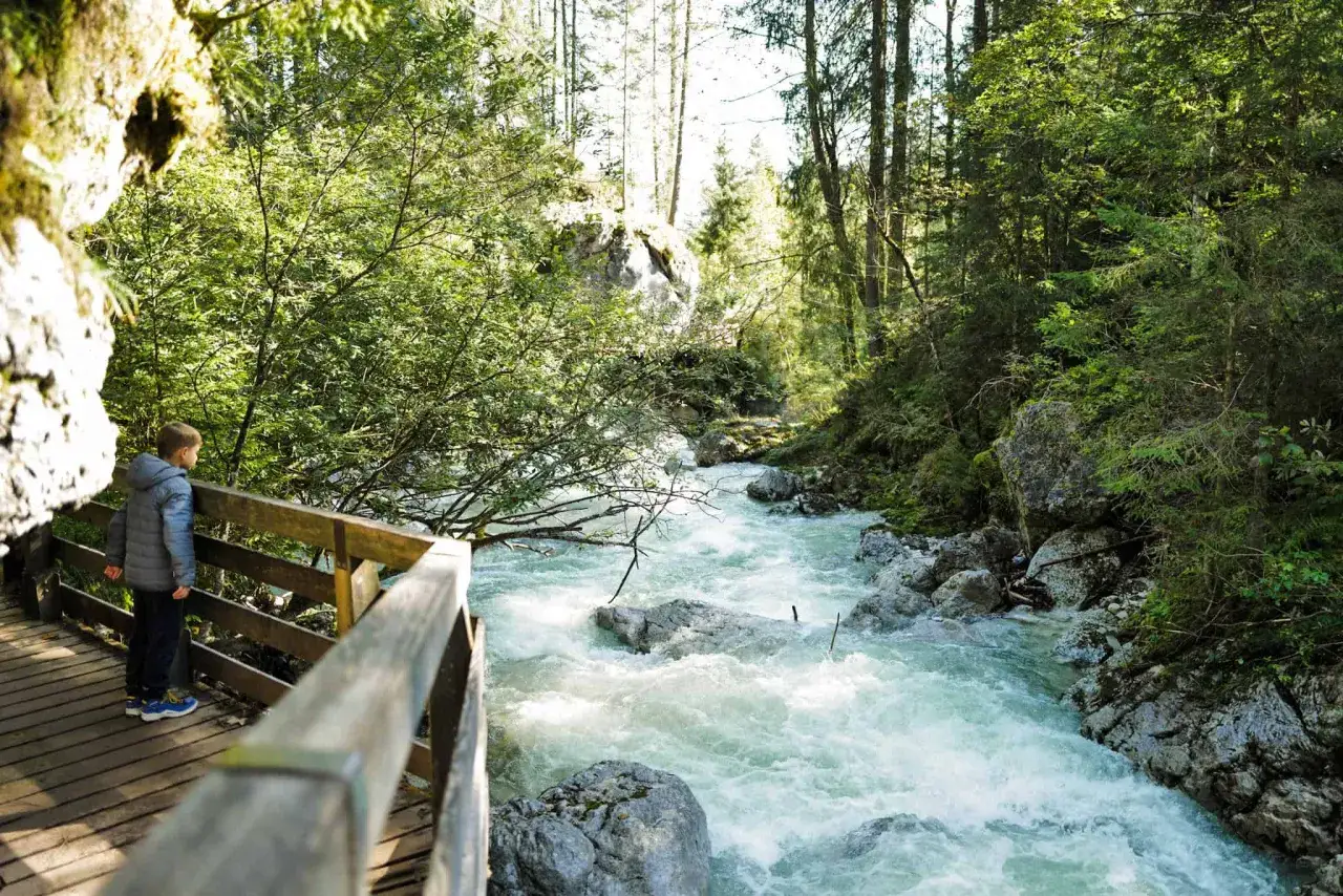 Ein Junge steht auf einem Holzsteg und blickt auf einen tosenden Bach im zauberwald berchtesgaden.