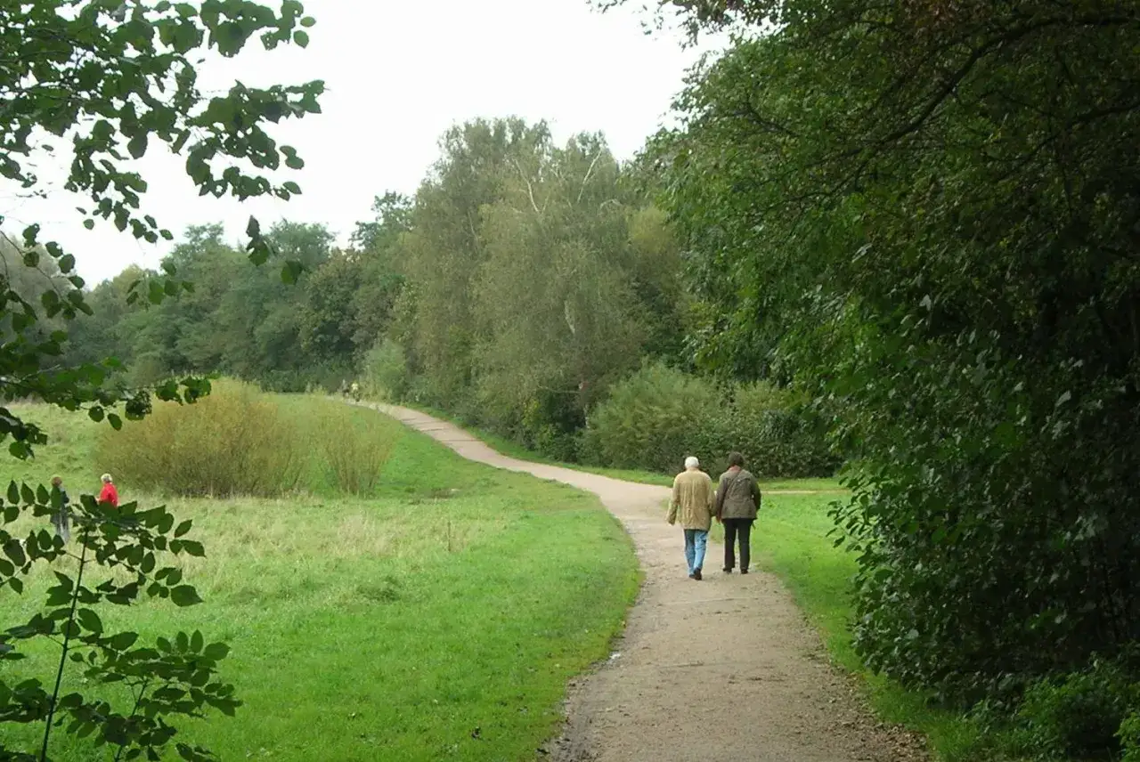 Zwei Personen spazieren auf einem Weg durch eine gr&uuml;ne Landschaft, die an die Stellinger Schweiz erinnert.