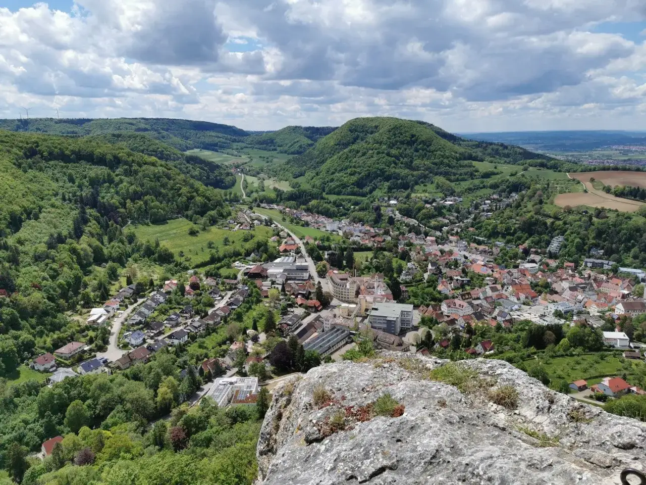 Blick vom Felsen auf die Stadt unterhalb der Ruine Rosenstein, umgeben von gr&uuml;nen H&uuml;geln und bew&ouml;lktem Himmel.