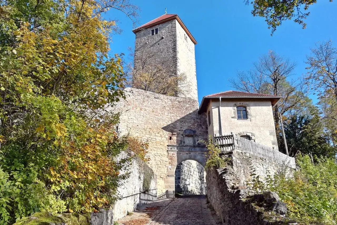Herbstliche Farben umgeben die imposante Lichtenburg in Ostheim. Ein steinernes Tor führt zu einem Wehrgang.