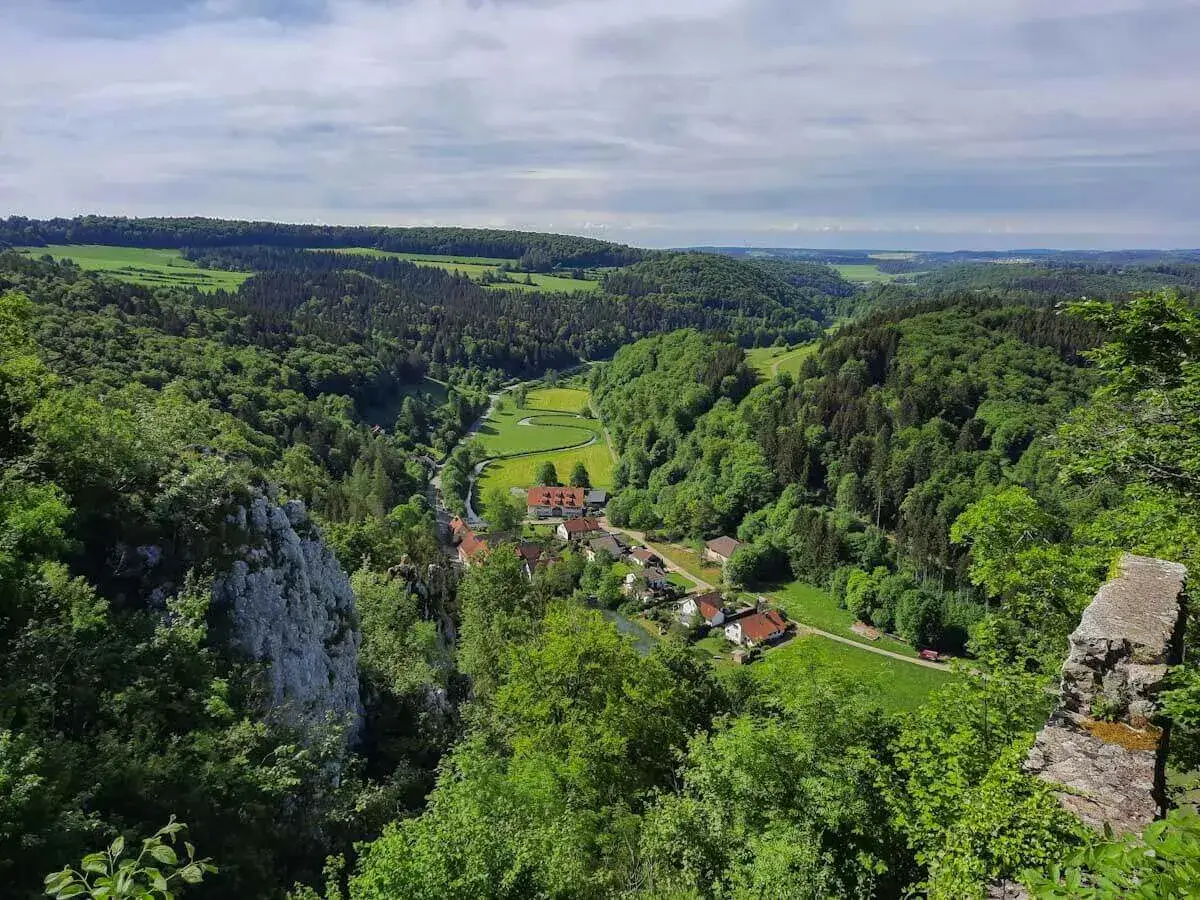 Grünes Lautertal Alb mit einem kleinen Dorf, umgeben von Wäldern und Feldern. Ein Fluss schlängelt sich durch das Tal.