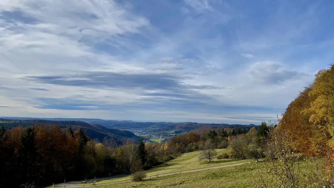 Herbstliche Hügellandschaft bei Welzheim, mit bunten Bäumen und einem Tal im Hintergrund. Die Wolken am Himmel scheinen wie feenspuren.