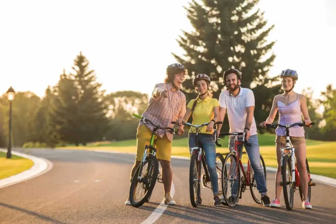 Vier junge Leute mit Fahrrädern und Helmen genießen eine Fahrradtour mit Kindern im sonnigen Park.