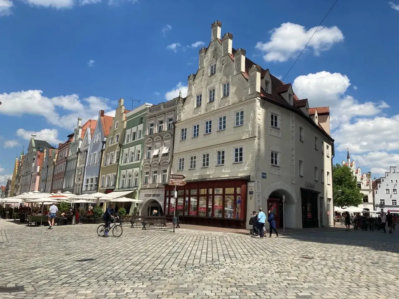 Bunte Giebelhäuser säumen den Platz, ein Radfahrer fährt vorbei. Hier gibt es viele Landshut Geheimtipps zu entdecken.