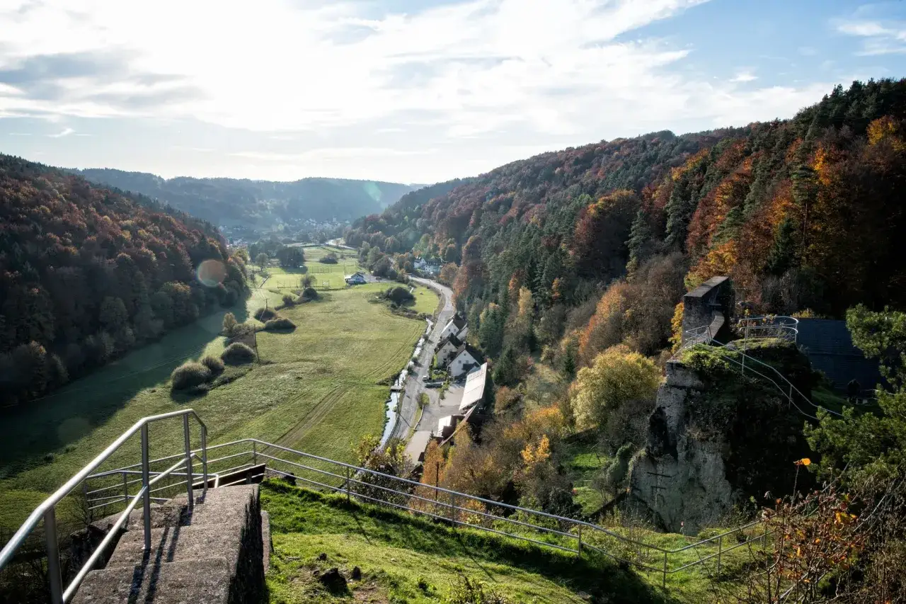 Blick auf die Burgruine Wolfsberg im Herbst. Ein malerisches Tal mit bunten W&auml;ldern, gr&uuml;nen Wiesen und einem kleinen Dorf.