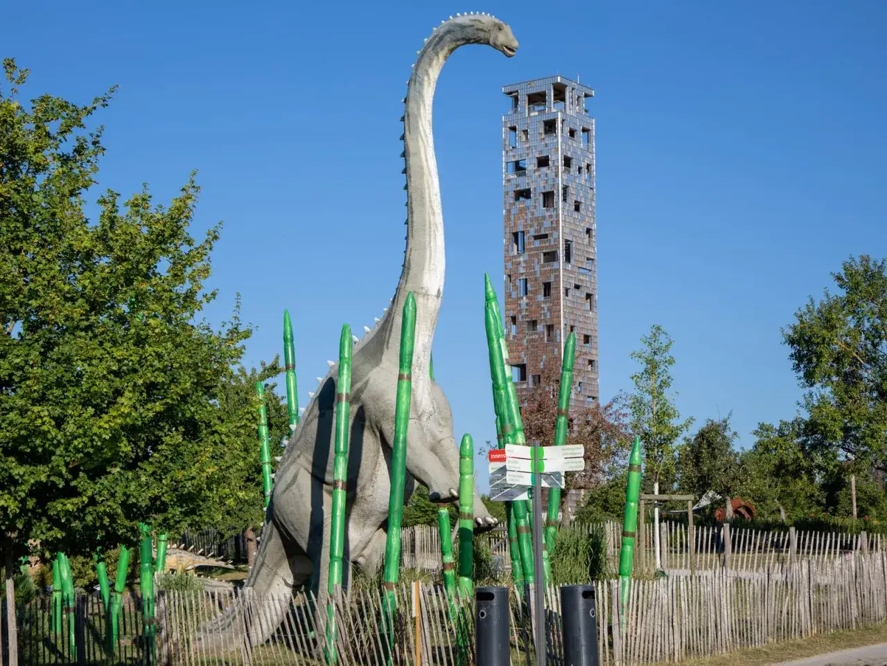 Ein riesiger Dinosaurier-Nachbau steht zwischen gr&uuml;nen Bambus-Stangen. Im Hintergrund ragt ein moderner Turm auf. Ein Hauch von Urzeit im Himmelsgarten.