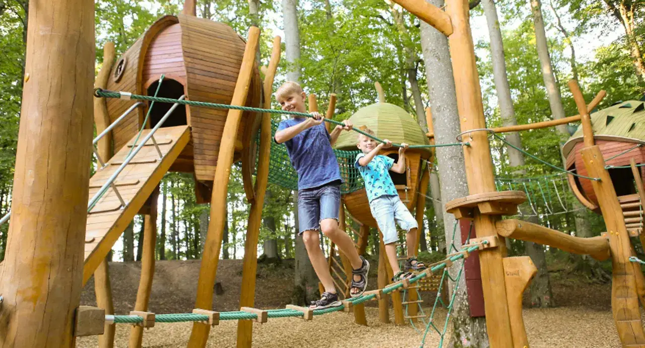 Zwei Jungen balancieren über Seilbrücken auf einem Baumhaus-Spielplatz. Ein tolles Erlebnis für Kinder!