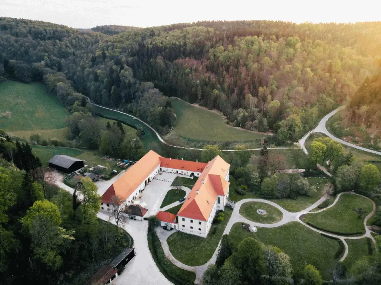 Schloss Ehrenfels bei Hayingen, ein weitläufiger Gebäudekomplex mit roten Dächern, eingebettet in eine grüne Hügellandschaft mit Wäldern und Wiesen.