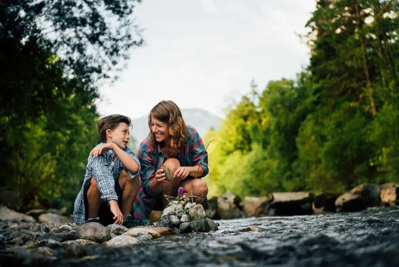 Mutter und Sohn bauen am Flussufer einen Steinturm. Ein schöner Tag am Tegernsee mit Kindern.