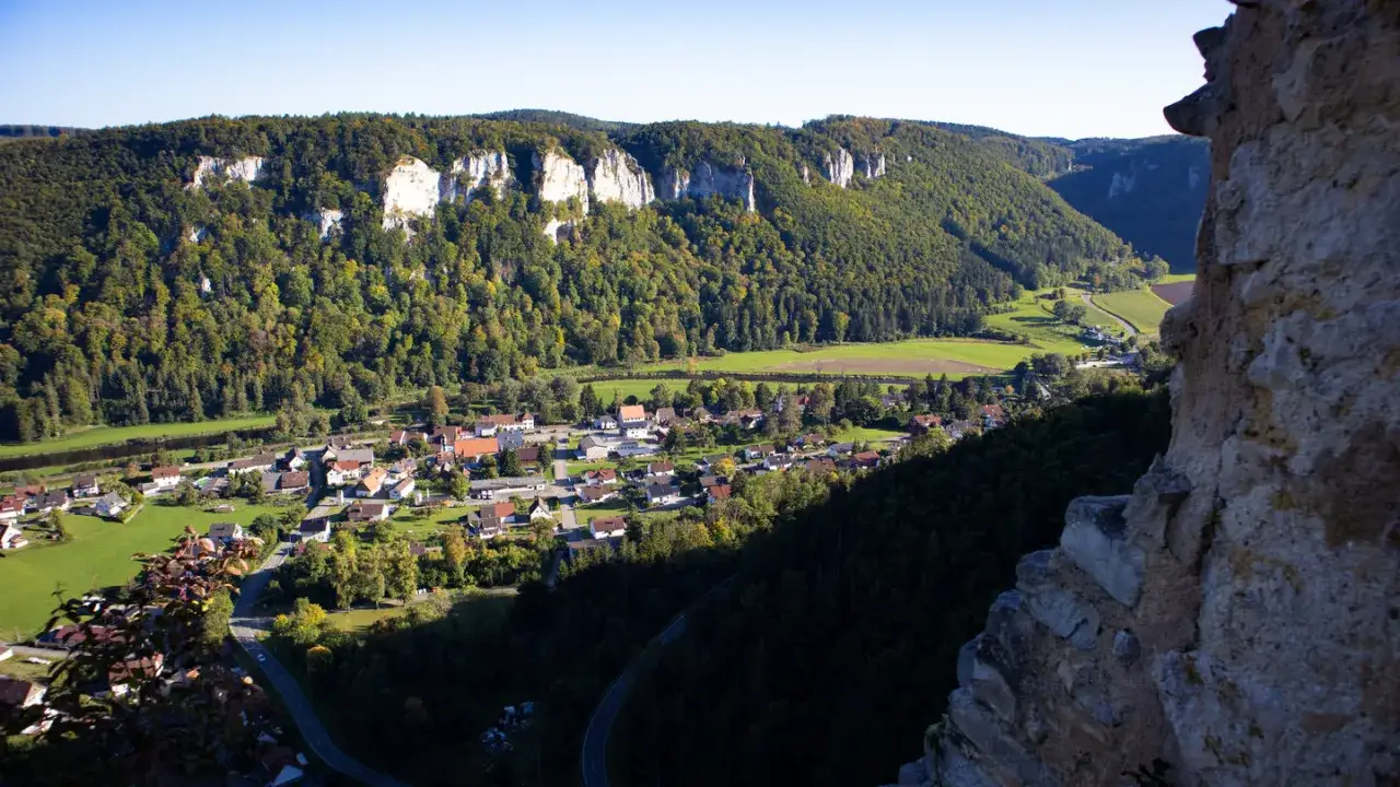 Blick von der ruine kallenberg auf ein malerisches Dorf im Tal, umgeben von bewaldeten H&auml;ngen und Felsformationen.