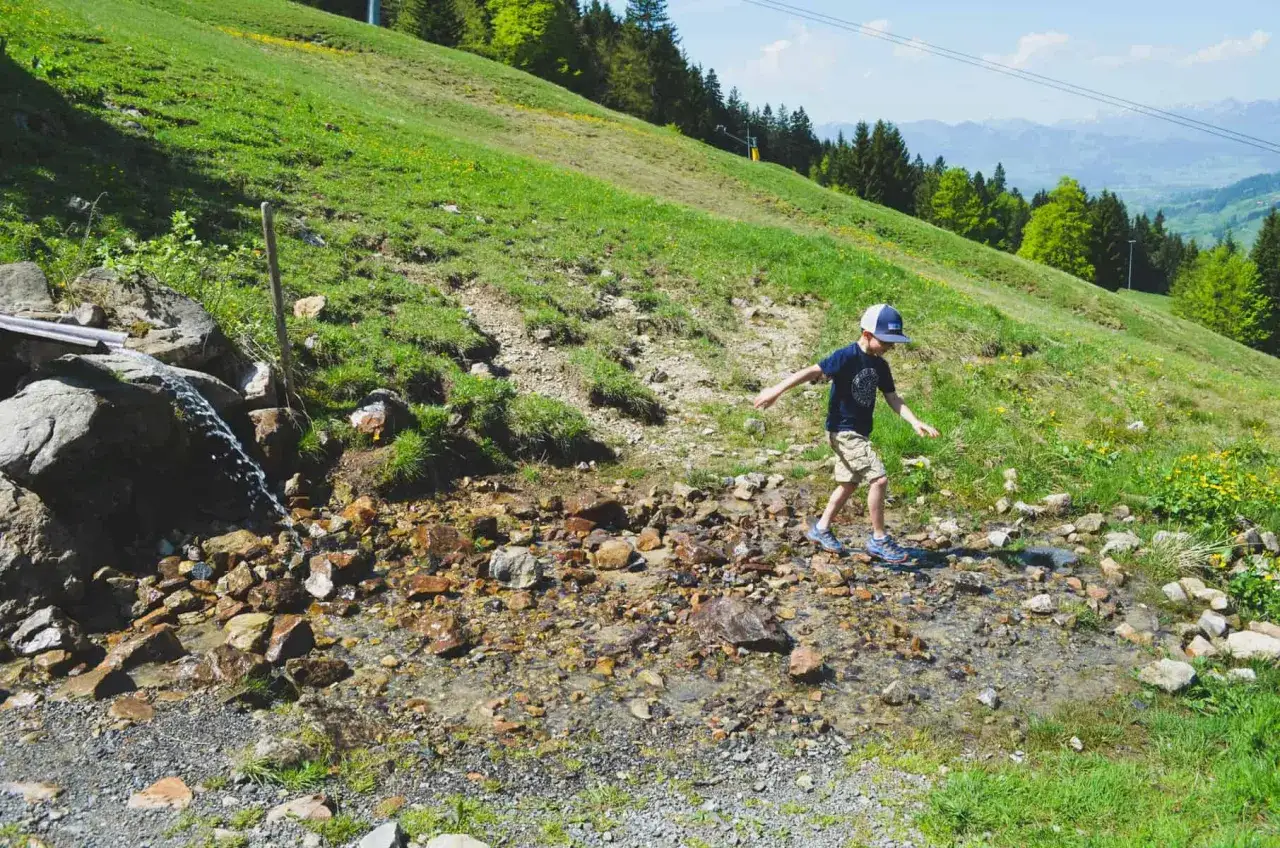 Ein Junge balanciert über Steine in einem Bachbett. Ein tolles Erlebnis beim Bad Hindelang wandern mit Kindern im Grünen.