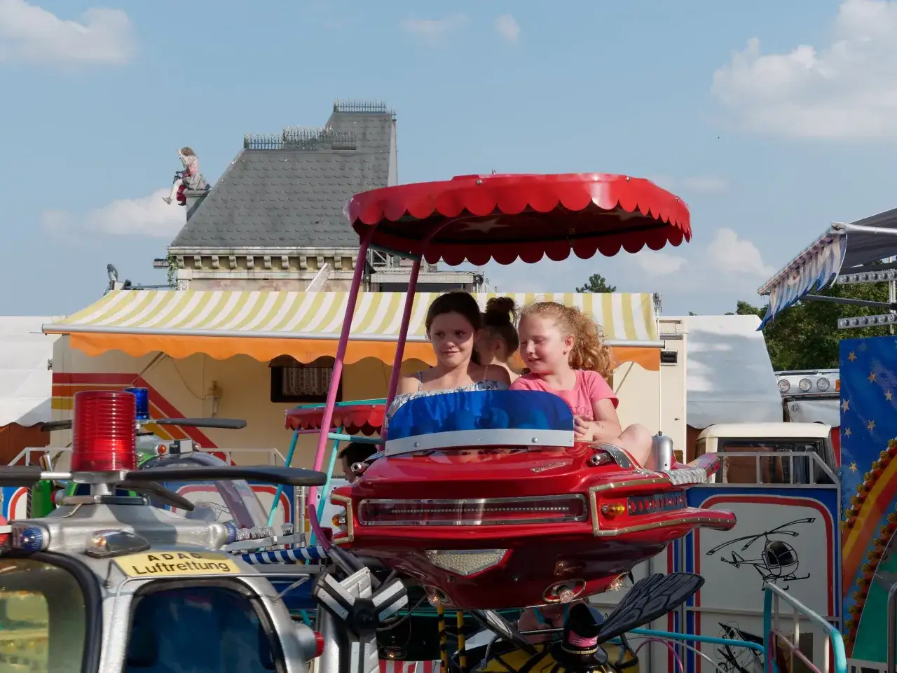 Zwei M&auml;dchen auf einem Fahrgesch&auml;ft in Regensburg mit Kindern. Ein rotes Flugzeug mit Propellern und Blaulicht.