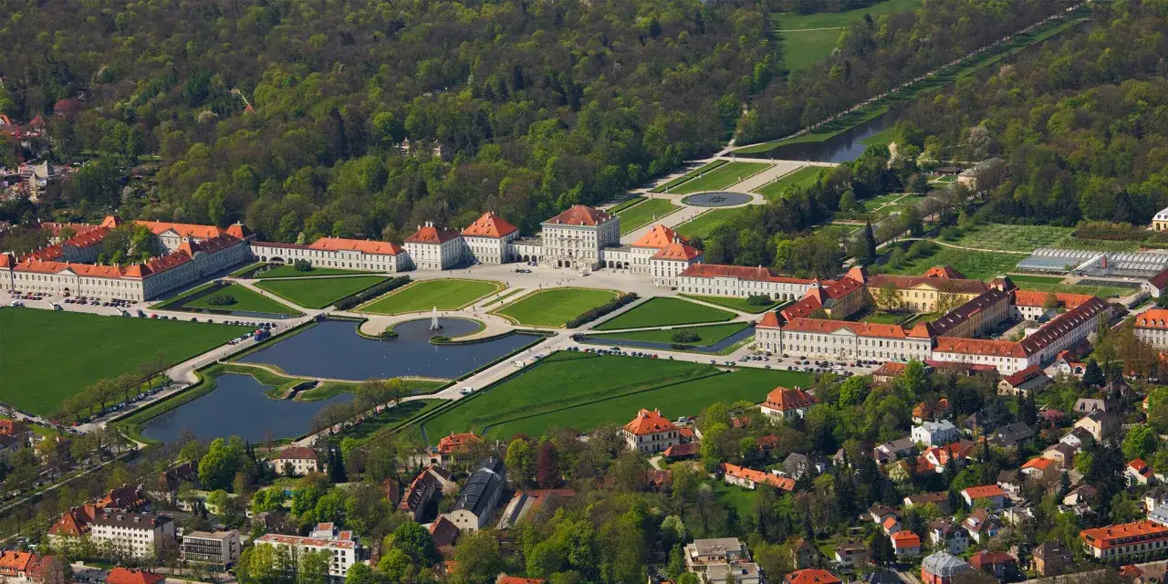 Luftaufnahme des Schlosses Nymphenburg, einer prächtigen Burg Bayerns, mit weitläufigen Gärten, Seen und umliegenden Gebäuden.
