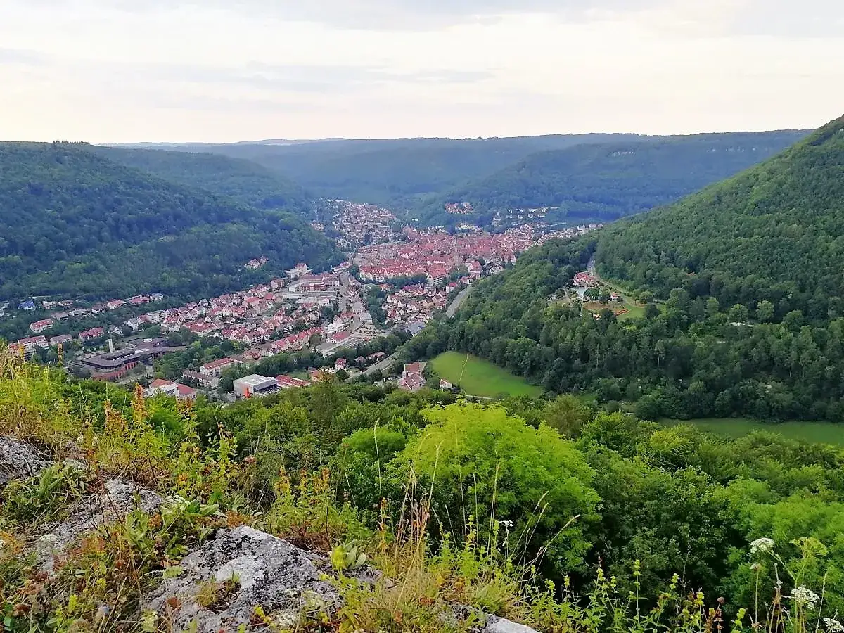 Blick vom Felsen auf das Tal mit der Stadt und den Wäldern. Die Burg Hohenurach thront majestätisch über der Landschaft.