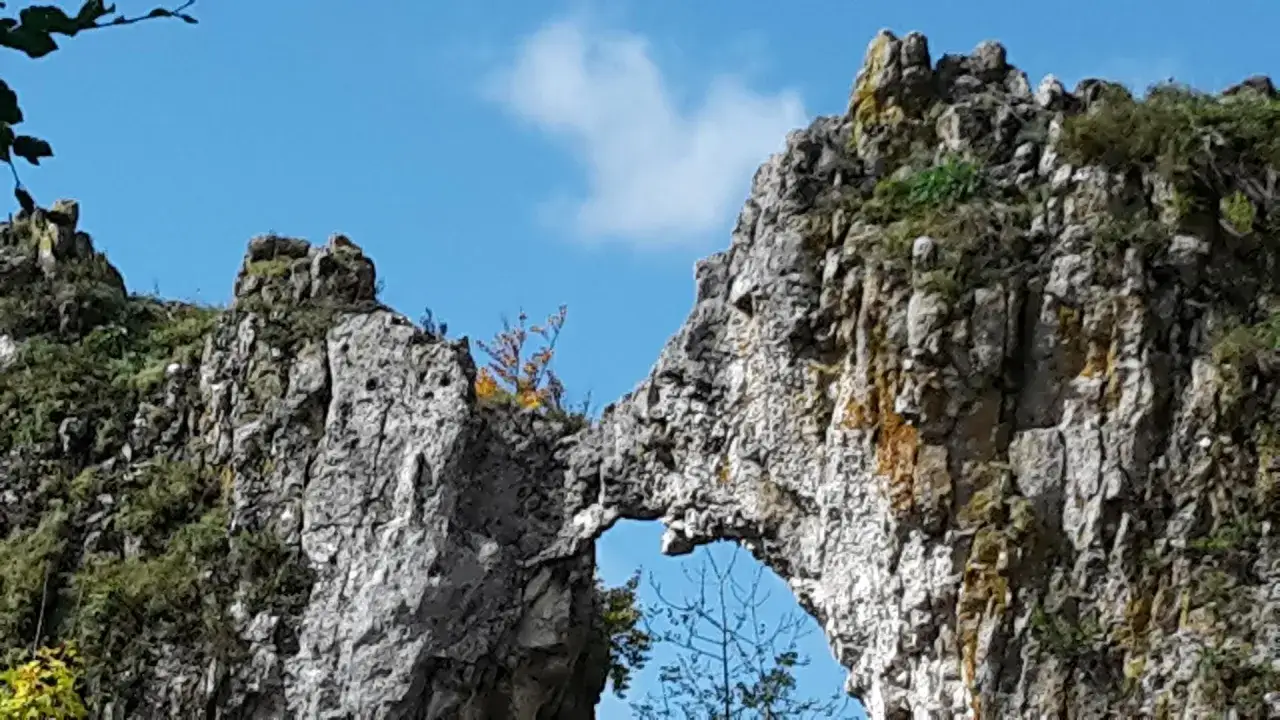Felsenlabyrinth Blaubeuren: Ein natürliches Felsentor mit zerklüfteten Felsen und grüner Vegetation unter blauem Himmel.