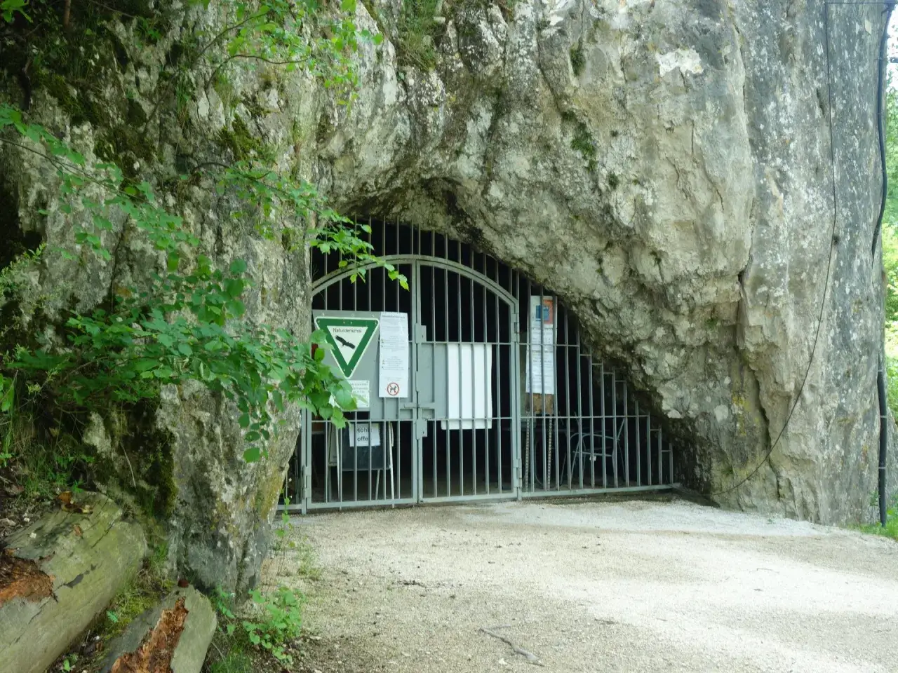 Eingang zu einer H&ouml;hle mit Gittertor, Hinweisschildern und dem Hinweis 
