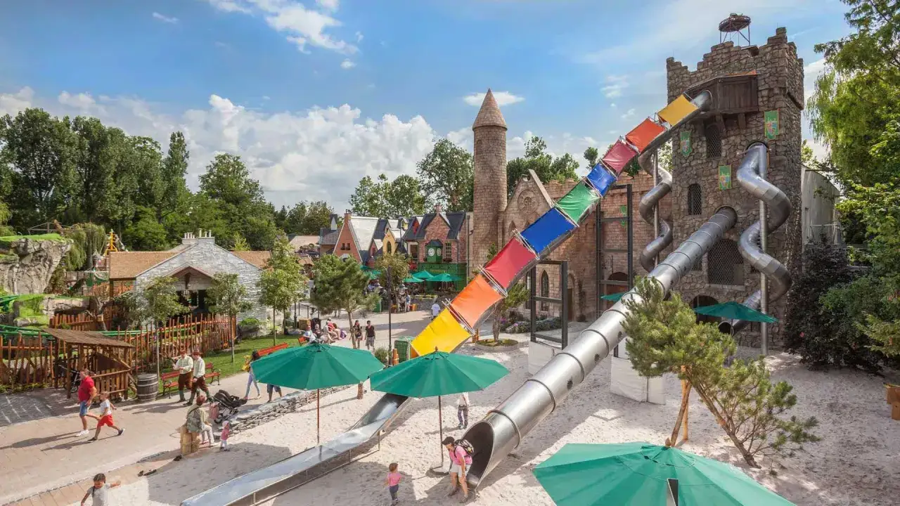 Bunter, mehrstufiger Spielplatz im Europa-Park mit Rutschen, die von einem steinernen Turm herabf&uuml;hren. Kinder spielen im Sand.