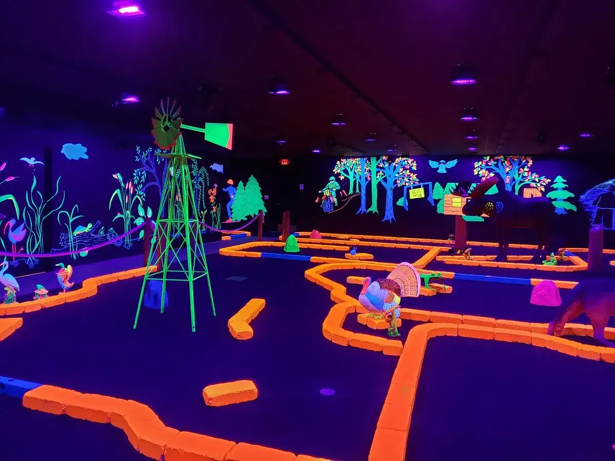 Ein leuchtendes indoor schwarzlicht minigolf Abenteuer mit bunten Hindernissen, einer Windmühle und Tierfiguren.
