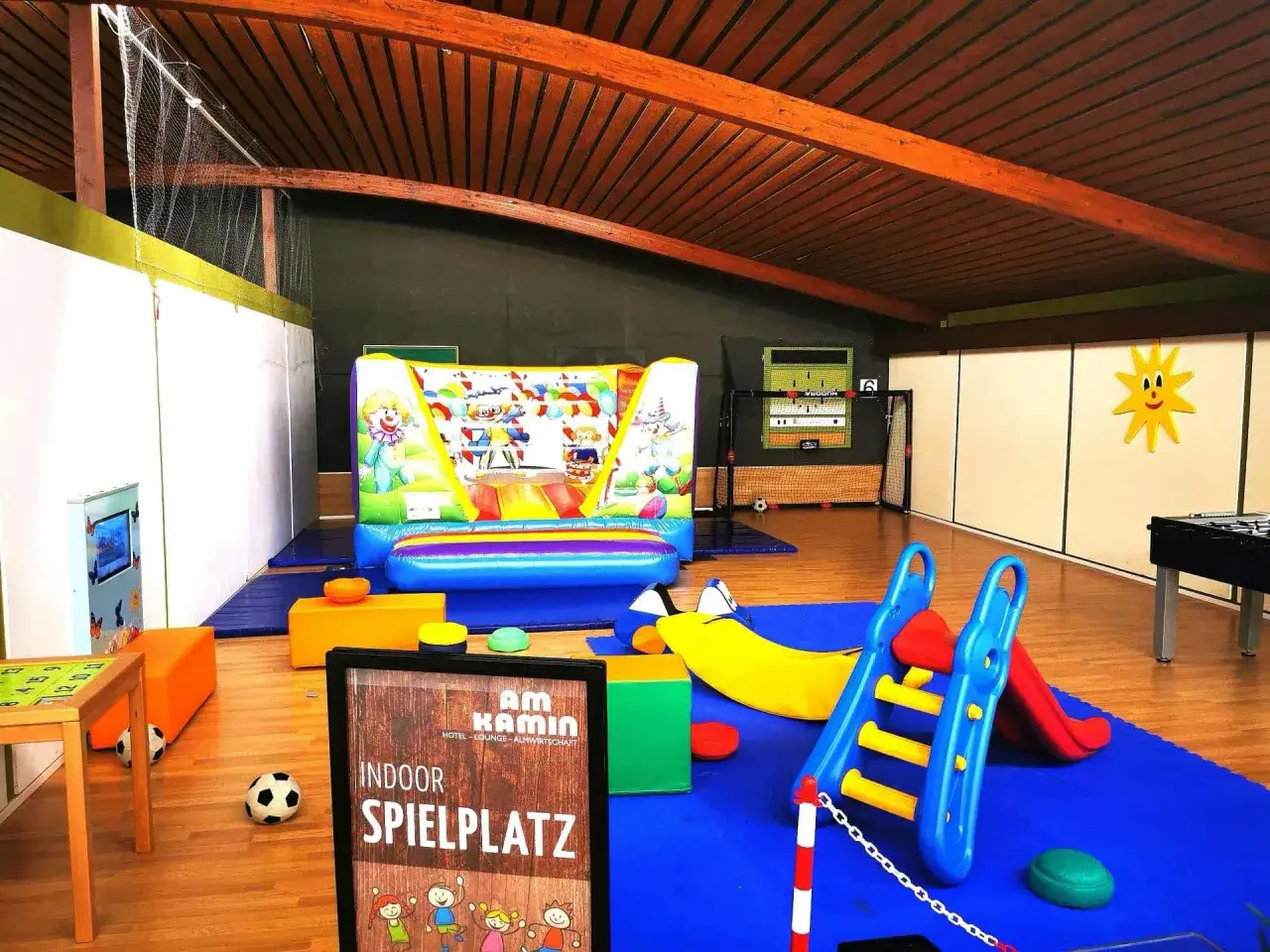 Ein bunter Indoor-Spielplatz mit Hüpfburg, Rutsche und Spielgeräten. Perfekt für Kinder, während Eltern im angrenzenden Cafe entspannen.
