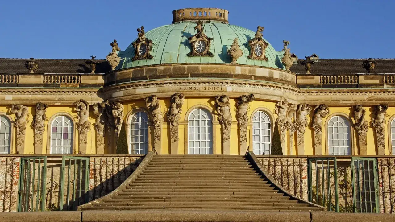 SANS SOUCI: Ein Schloss in Brandenburg, das wie eine Ritterburg f&uuml;r Kinder wirkt. Die Fassade ist gelb, mit einer gr&uuml;nen Kuppel und vielen Statuen.