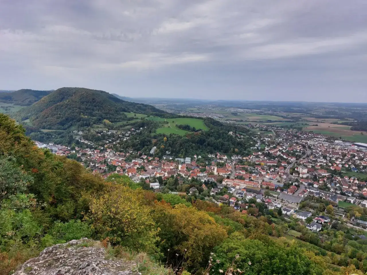 Blick von einem Felsen auf Heubach, das sich ins Tal schmiegt. Ein Wanderer genie&szlig;t die Aussicht auf die herbstliche Landschaft und die Stadt.