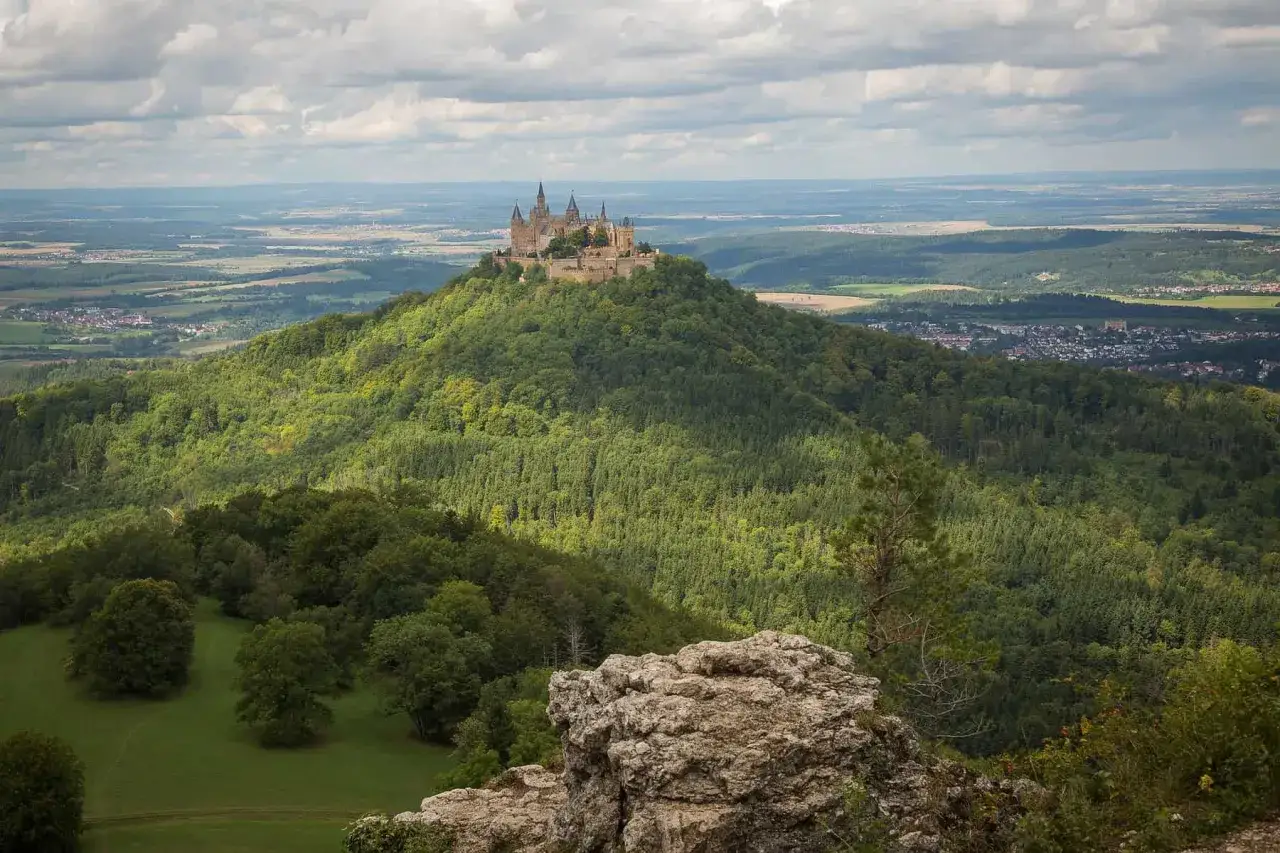 Blick vom Aussichtspunkt auf die Burg Hohenzollern, majestätisch auf einem grünen Berg thronend, umgeben von Wäldern und einer weiten Landschaft.