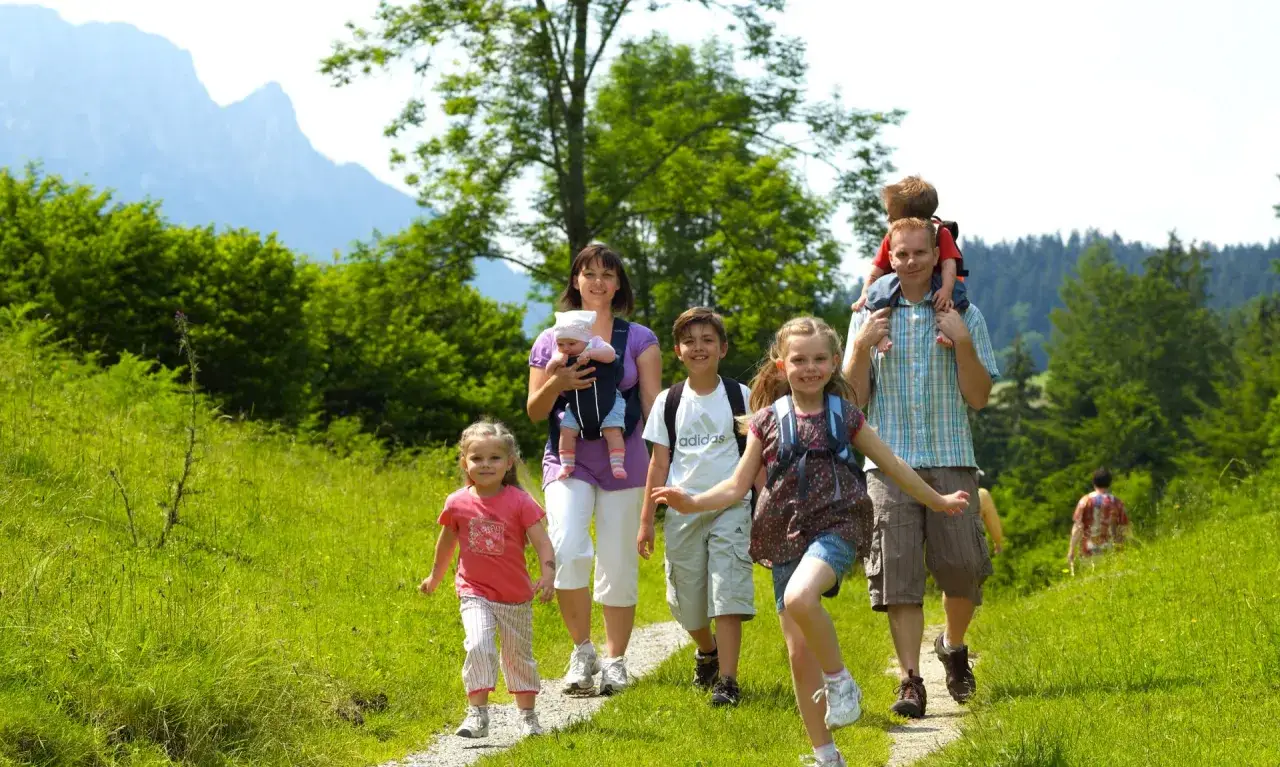 Familie genie&szlig;t eine leichte Wanderung mit Kindern in Bayern. Sonnenschein, gr&uuml;ne Wiesen und Berge im Hintergrund.
