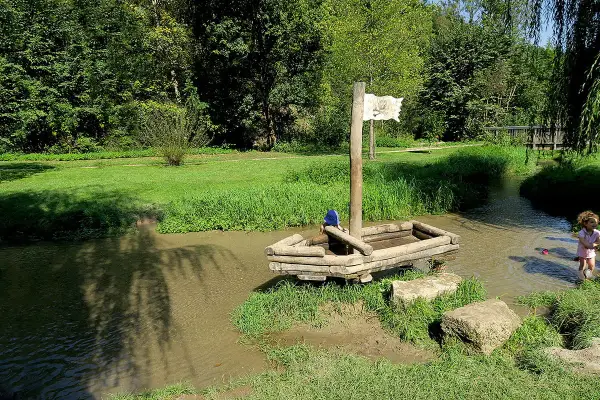 Ein hölzernes Piratenschiff mit einem Kind an Bord im Wolfstal Lauterach. Ein weiteres Kind spielt im Wasser.