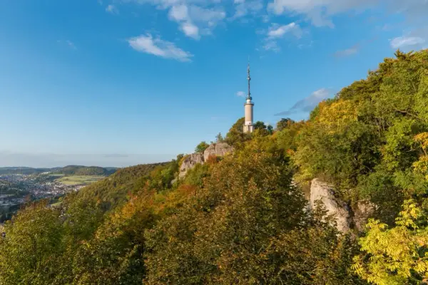 Der Schlossfelsenturm Albstadt ragt auf einem bewaldeten Felsen über der Stadt auf. Bunte Herbstfarben schmücken die Hänge.